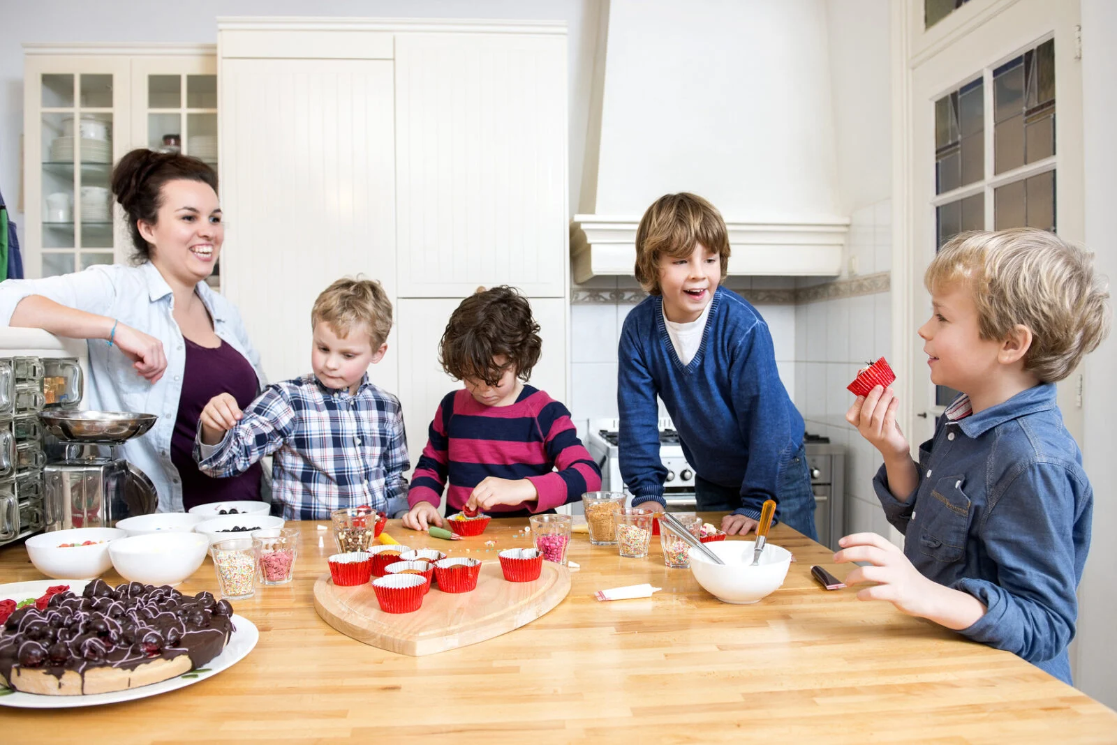 Children decorating cupcakes at a kitchen table with a woman