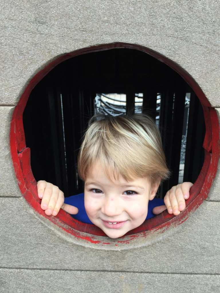 Smiling toddler peeking through a round window in a play structure