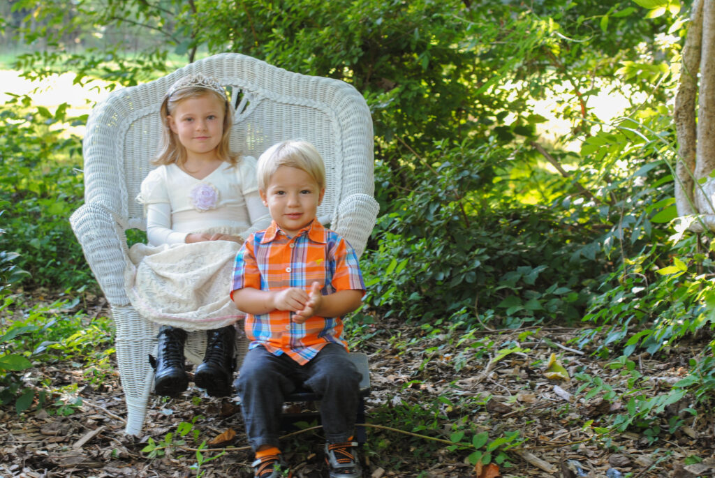 Toddler girl sitting in white chair and boy sitting on stool smiling.