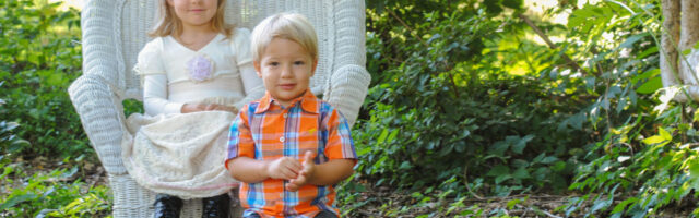 Toddler girl sitting in white chair and boy sitting on stool smiling.