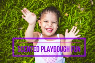 Smiling child lying on grass with text: Scented Playdough Fun