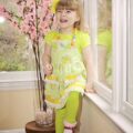 A happy young girl in a bright green dress and yellow headband, smiling widely, representing the joy and positive environment found with Georgia's Dream Nannies.