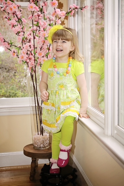 A happy young girl in a bright green dress and yellow headband, smiling widely, representing the joy and positive environment found with Georgia's Dream Nannies.
