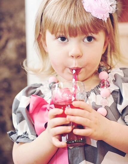 A little girl drinks pink punch.