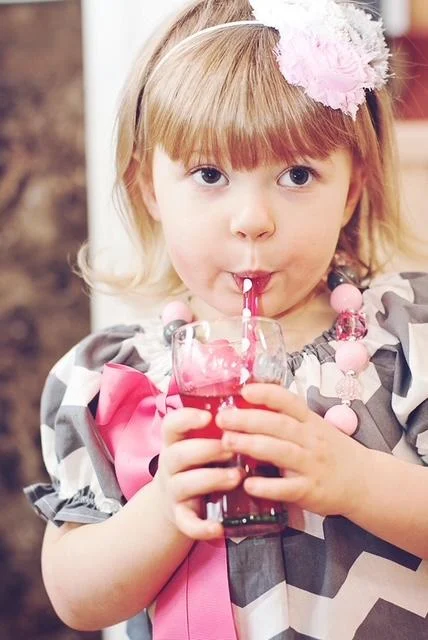 A little girl drinks pink punch.