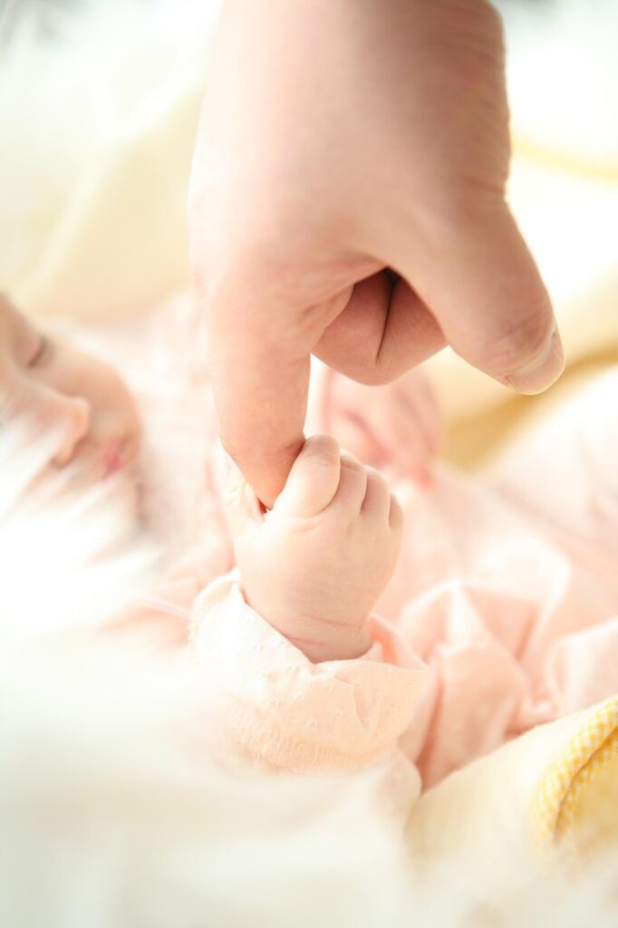 A newborn baby gently holding an adult’s finger while resting.