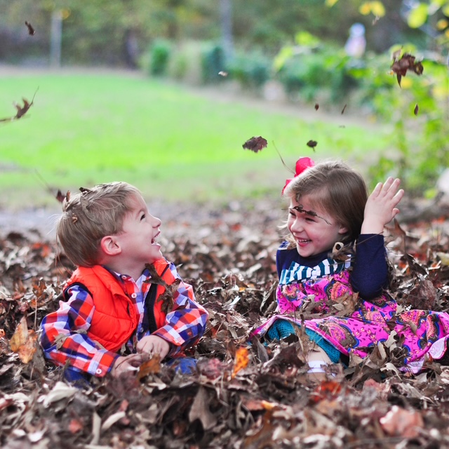 Two children laughing and playing in autumn leaves - Dream Nannies Trusted Household Staffing